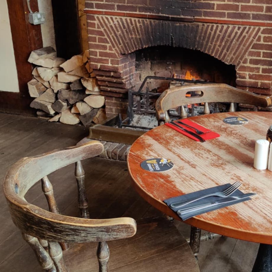Cosy interior of The Dukes Head pub in Hamstreet, Kent, with a dining table set beside a fireplace